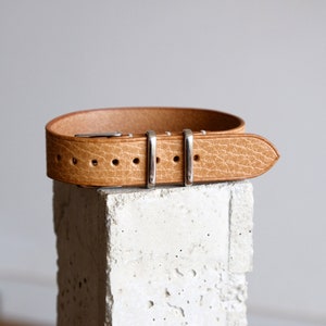 May include: A tan leather watch strap with silver buckle and keepers.