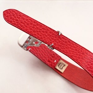 May include: Red leather watch strap with a silver buckle and a small logo on the strap.