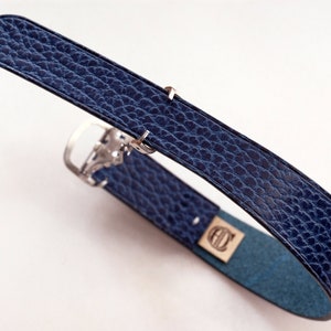 Könnte beinhalten: Ein dunkelblaues Lederarmband mit einer silbernen Schließe. Das Armband hat eine strukturierte Oberfläche und ist zu einem Kreis gefaltet.