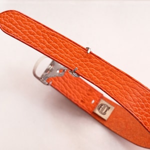 May include: Orange leather watch band with a silver buckle.