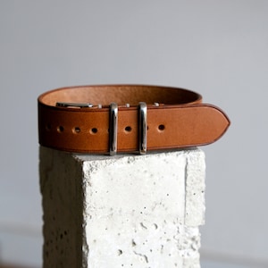 Puede incluir: Una correa de reloj de cuero marrón con hebilla y pasadores plateados.