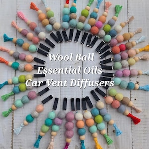 May include: A collection of car vent diffusers arranged in a circle, each featuring a black clip attached to a string of colorful felt wool balls and a small tassel. The text Wool Ball Essential Oils Car Vent Diffusers is centered.