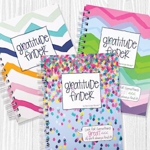 May include: Three different gratitude journals with colorful covers. The covers feature a confetti pattern, a chevron pattern, and a mountain range pattern. Each journal has the text "gratitude finder" on the cover.
