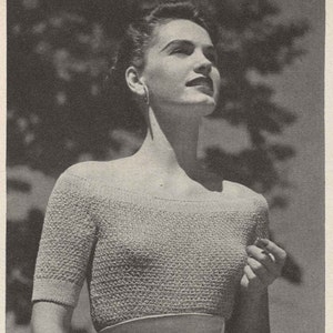 Puede incluir: Una foto en blanco y negro de una mujer con una blusa de noche de cuello redondo con un cinturón de cinta. La blusa está tejida y tiene un patrón texturizado. La mujer está de pie frente a un árbol.