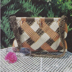 May include: A brown, white, and orange crocheted bag with a diamond pattern. The bag has a long strap and is sitting on a white metal table.
