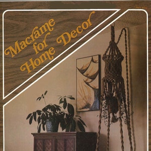 Puede incluir: Una portada de libro con el título "Macramé para la decoración del hogar" en una fuente marrón y naranja. La portada presenta un macramé colgante para plantas con una base de madera, una planta de interior y un armario de madera con una puerta estampada.
