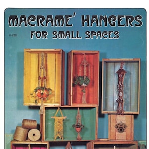 May include: A book cover with the title "Macrame' Hangers for Small Spaces" and the number H-228. The cover features a colourful display of macrame plant hangers in various styles and colours, hanging from wooden crates.