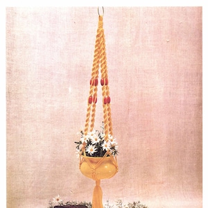 May include: A yellow macrame plant hanger with a ceramic pot filled with white flowers. The hanger is suspended from a metal ring and adorned with orange beads. The image includes text that reads "Materials Needed: 66 yards of Yellow Polyester Cable Cord... One 2 ½ inch solid metal ring."