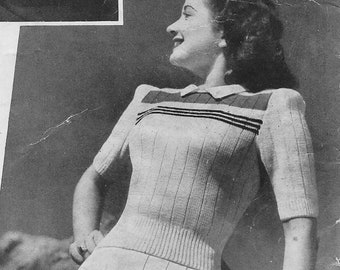 May include: A woman wearing a white knitted sweater with black and white stripes across the chest and a white skirt with a pleated front.