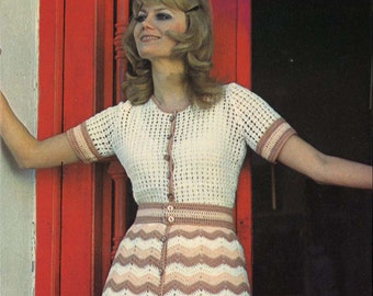 Könnte beinhalten: Ein weißes Häkelkleid mit einem braunen und weißen Zickzackmusterrock und kurzen Ärmeln. Das Kleid hat einen Knopfleisten vorne und einen Gürtel.