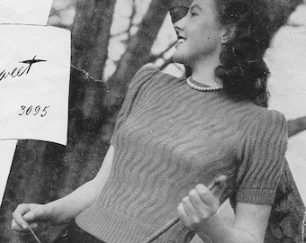 May include: A black and white photo of a woman wearing a knitted sweater with a cable knit pattern. The sweater has short sleeves and a round neckline. The woman is standing in front of a tree.