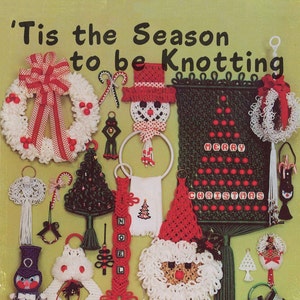 Puede incluir: Una portada de libro con el título 'Tis the Season to be Knotting' que presenta una variedad de artesanías navideñas hechas con nudos de macramé. Las artesanías incluyen una corona, un muñeco de nieve, un árbol de Navidad, un Papá Noel y una campana.