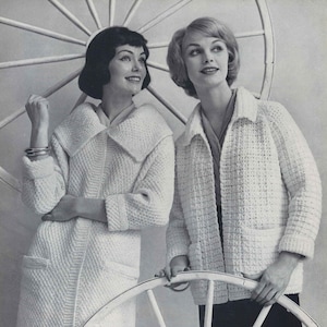 May include: Two women wearing white crocheted jackets. The woman on the left is wearing a long jacket with a large collar. The woman on the right is wearing a shorter jacket with a smaller collar. Both women are standing next to a white wooden wagon wheel.