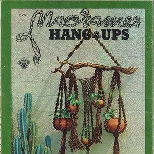 May include: A craft project pattern for macrame hang-ups. The pattern shows a macrame plant hanger with four pots and plants. The pattern is titled "Macrame Hang-Ups" and has the number H-213.