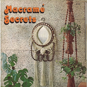 May include: A magazine cover featuring the title "Macrame Secrets" in orange letters. The cover features a macrame mirror with brown beads and a macrame plant hanger with brown tassels. The magazine cover also includes the text "Exciting new designs to brighten your home, including macra-weaving and macra-sculpture".