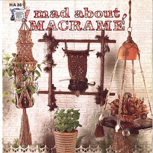May include: A vintage book cover with the title "mad about, MACRAME" in red and white lettering. The cover features a brick wall background with macrame wall hangings, plant hangers, and home accessories. The text "INCLUDES POT HANGERS - JEWELRY - WALL HANGINGS & HOME ACCESSORIES" is printed at the bottom of the cover.