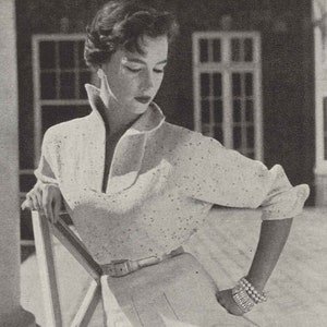 May include: A white knitted blouse with batwing sleeves and a V-neck collar. The blouse is made with metallic yarn and has a belt around the waist.