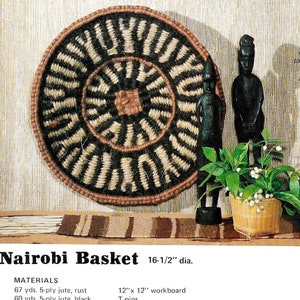 May include: A round, woven basket with black and brown stripes. The basket is 16 1/2 inches in diameter and is made of jute. The basket is hanging on a wall with a wooden statue and a potted plant in front of it.
