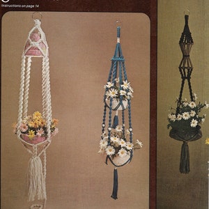 May include: Two macrame plant hangers with white and blue rope, each with a white ceramic pot and white flowers. The macrame plant hangers are titled "Patchwork Light Contessa" and "Fitz-E-E".