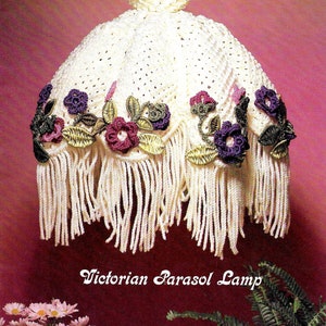 May include: A white crocheted lampshade with a fringe border and floral accents in shades of purple, green, and pink. The lampshade is labeled "Victorian Parasol Lamp".
