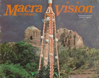 May include: Vintage magazine cover featuring a macrame plant hanger with a woven basket holding green plants. The hanger is orange and white, with wooden beads. The background shows a scenic view of a river and mountains. Text reads "Macra Vision".