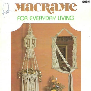 May include: A vintage book cover for a macrame craft book. The cover features a beige macrame hanging planter with gold-colored fruit, a macrame mirror, and the text "Macrame for Everyday Living".