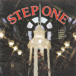 May include: A white macrame table lamp with a diamond cross pattern. The lamp is hanging from a ceiling and has a white cord. The text "STEP ONE" is in red letters at the top of the image. The text "DIAMOND CROSS TABLE (Pattern on page 12)" is at the bottom of the image.