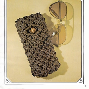 May include: A brown crocheted eyeglasses case with a wooden button closure. The case is lying on a beige surface next to a pair of brown sunglasses.