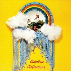 Puede incluir: Una pared colgante de hilo de color arcoíris con un espejo en el centro. La pared colgante tiene nubes blancas y esponjosas y flecos de hilo azul. El texto "Rainbow Reflections" está escrito debajo de la pared colgante. Se incluyen instrucciones para hacer la pared colgante.