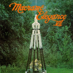 May include: A white macrame plant hanger with a brown wooden ring at the top and a brown base. The hanger is hanging from a hook in a green grassy area. The text "Macrame Elegance III" is visible in the top right corner of the image. The text "La Couronne" is visible in the bottom center of the image.