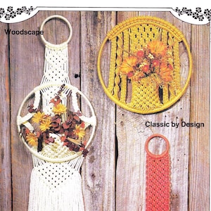 以下が含まれることがあります： 木製の背景に、マクラメの壁掛けが3つあります。壁掛けは、円形、長方形、涙の形をしています。円形は黄色い花のアレンジメントで白く、長方形は黄色い花のアレンジメントで黄色く、涙は白い花のアレンジメントで赤いです。各壁掛けの下には、「Woodscape」、「Classic by Design」、「Flamenco」というテキストが書かれています。