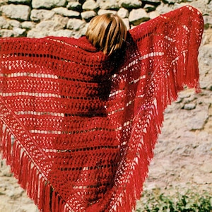 Puede incluir: Un chal de ganchillo rojo con flecos. El chal está hecho con un punto de encaje y tiene una forma triangular.