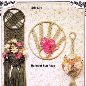 以下が含まれることがあります： 花柄のアクセントが付いたマクラメの壁掛けが3つ。1つ目は、円形のデザインと「静物」というタイトルの緑色の壁掛け。2つ目は、円形のデザインと「太陽の光のバレエ」というタイトルのベージュ色の壁掛け。3つ目は、円形のデザインと「春のオード」というタイトルのベージュ色の壁掛けです。