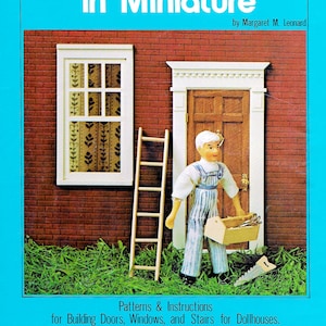 May include: A book cover with the title "Trim Carpentry in Miniature" by Margaret M. Leonard. The cover features a dollhouse exterior with a window, door, and a miniature carpenter holding a toolbox and saw. The book includes patterns and instructions for building doors, windows, and stairs for dollhouses in a 1:12 scale.