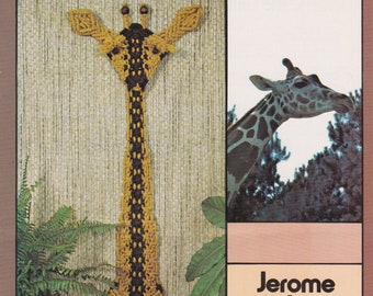 May include: A brown and yellow macrame giraffe wall hanging with a black tassel. The giraffe is hanging on a wall with a fern plant in the background. The text "Jerome the Giraffe" is printed on a brown and pink background.