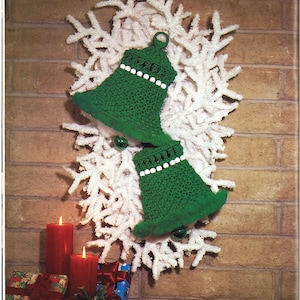 Puede incluir: Dos campanas de ganchillo verdes con cuentas blancas colgando de una corona blanca y esponjosa en forma de copo de nieve en una pared de ladrillo. Dos velas rojas y regalos envueltos se encuentran en la esquina inferior izquierda. El texto "Rhapsody in Bells - Page 10" está debajo de la corona.