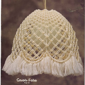 May include: A white macrame lampshade with a fringe trim. The lampshade is hanging from a white cord. The text "Savoir-Faire Page 22" is printed below the lampshade.