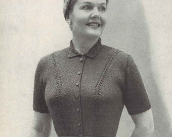 May include: A woman wearing a dark gray knitted dress with short sleeves, a collared neckline, and a matching belt. The dress has a button-down front and a flared skirt. She is also wearing a headscarf, earrings, and gloves, and carrying a small purse.