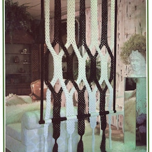 Może przedstawiać: Makrama dzieląca pokój z naprzemiennymi czarno-białymi panelami tkanymi. Panele są zawieszone na poziomej drewnianej listwie i mają dekoracyjne frędzle na dole. Dzielnik jest elementem dekoracyjnym.