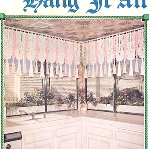 May include: A pink and white macrame curtain with tassels hangs in a kitchen with white cabinets and a double sink. The title "Juliano's Hang It All Book 4 Sweet and Sassy" is printed on the page.