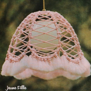 May include: A pink macrame lampshade with a fringe border. The lampshade is hanging from a string.