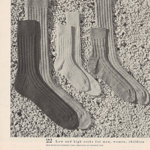 Könnte beinhalten: Drei Paar Socken in verschiedenen Längen, aus einem strukturierten Strickstoff. Die Socken sind auf einem Hintergrund aus kleinen weißen Steinen angeordnet. Der Text "SOCKS" ist unten im Bild in Schwarz gedruckt.