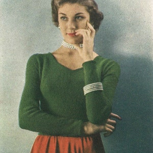 May include: A woman wearing a green sweater with a red skirt and a pearl necklace. She is looking to the side and has her hand on her chin.
