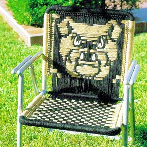 Puede incluir: Una silla tejida negra y marrón con un diseño de cara de cerdo en el respaldo. La silla es de metal y tiene un patrón de cuadros en el asiento.
