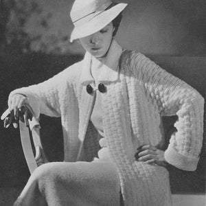Op de afbeelding: Een vrouw draagt een witte gebreide cardigan met een textuurpatroon en een witte hoed. De cardigan heeft grote knopen en een kraag.