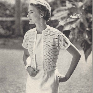 May include: A white crocheted cardigan with a delicate openwork pattern. The cardigan has short sleeves and a button-up front.