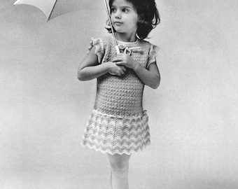 May include: A young girl wearing a white crocheted dress holds a white umbrella. She is wearing black shoes and has her hair tied back.