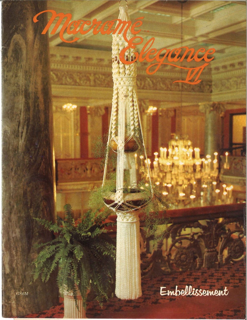 Peut inclure: Un porte-plante en macram&eacute; blanc avec un pompon, suspendu &agrave; un haut plafond dans une grande pi&egrave;ce. Le porte-plante est d&eacute;cor&eacute; d'une petite plante en pot. Le texte "Macrame Elegance II" est visible dans le coin sup&eacute;rieur droit de l'image. Le texte "Embellissement" est visible dans le coin inf&eacute;rieur droit de l'image.