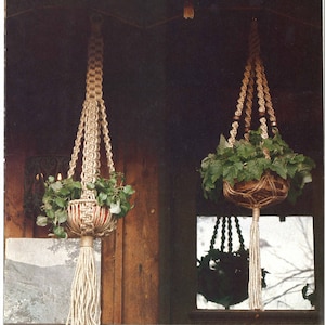 May include: Two macrame plant hangers with a natural rope design. The hangers are hanging from a wooden structure with a snowy roof. The hangers are holding green plants in brown pots. The text "Interessante Page 22" is on the left and "Au Naturel Page 22" is on the right.