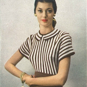 May include: A woman wearing a striped white and brown sweater with a brown skirt and a gold bracelet.